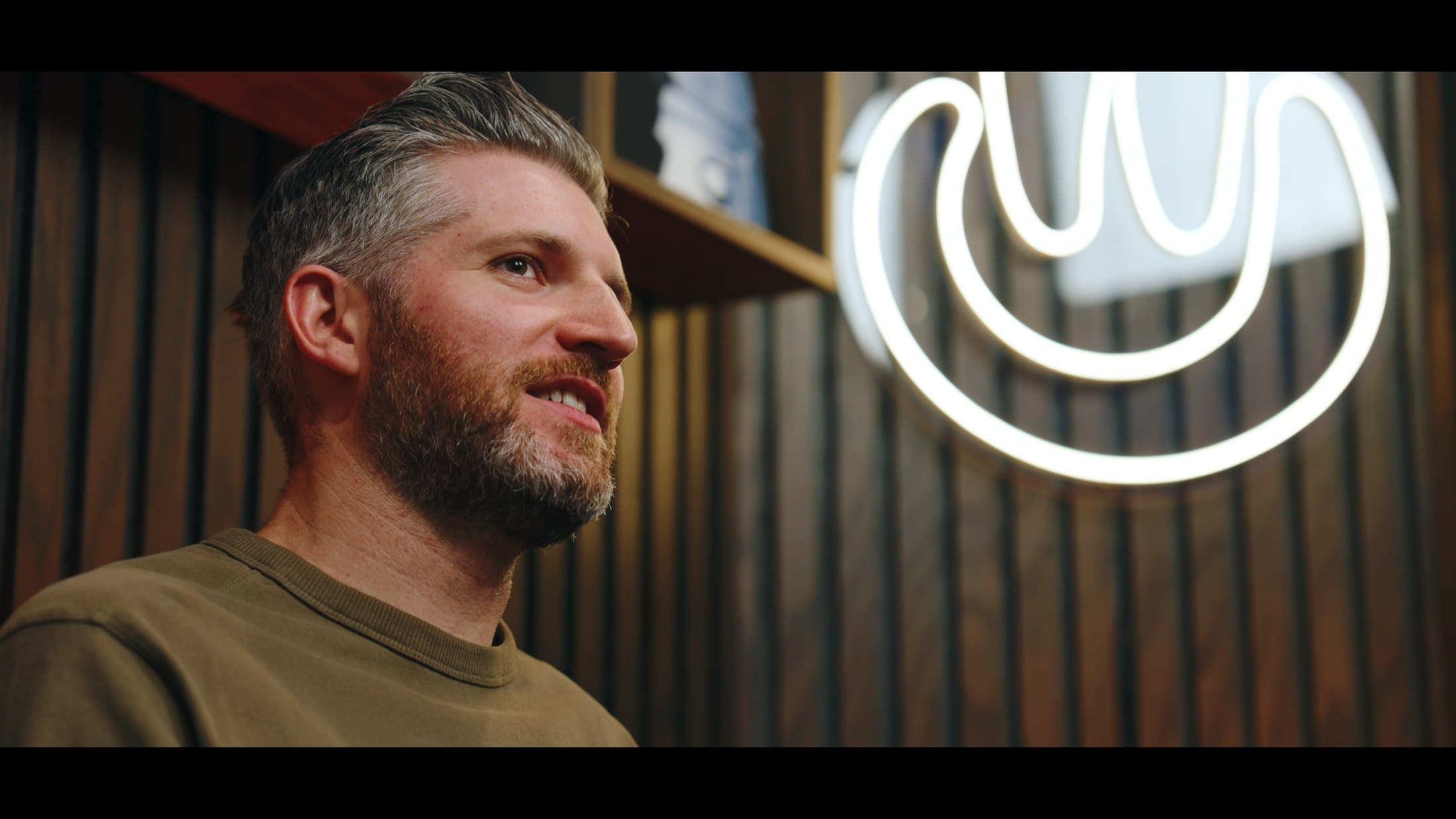 Profile portrait of the host beside a neon sign