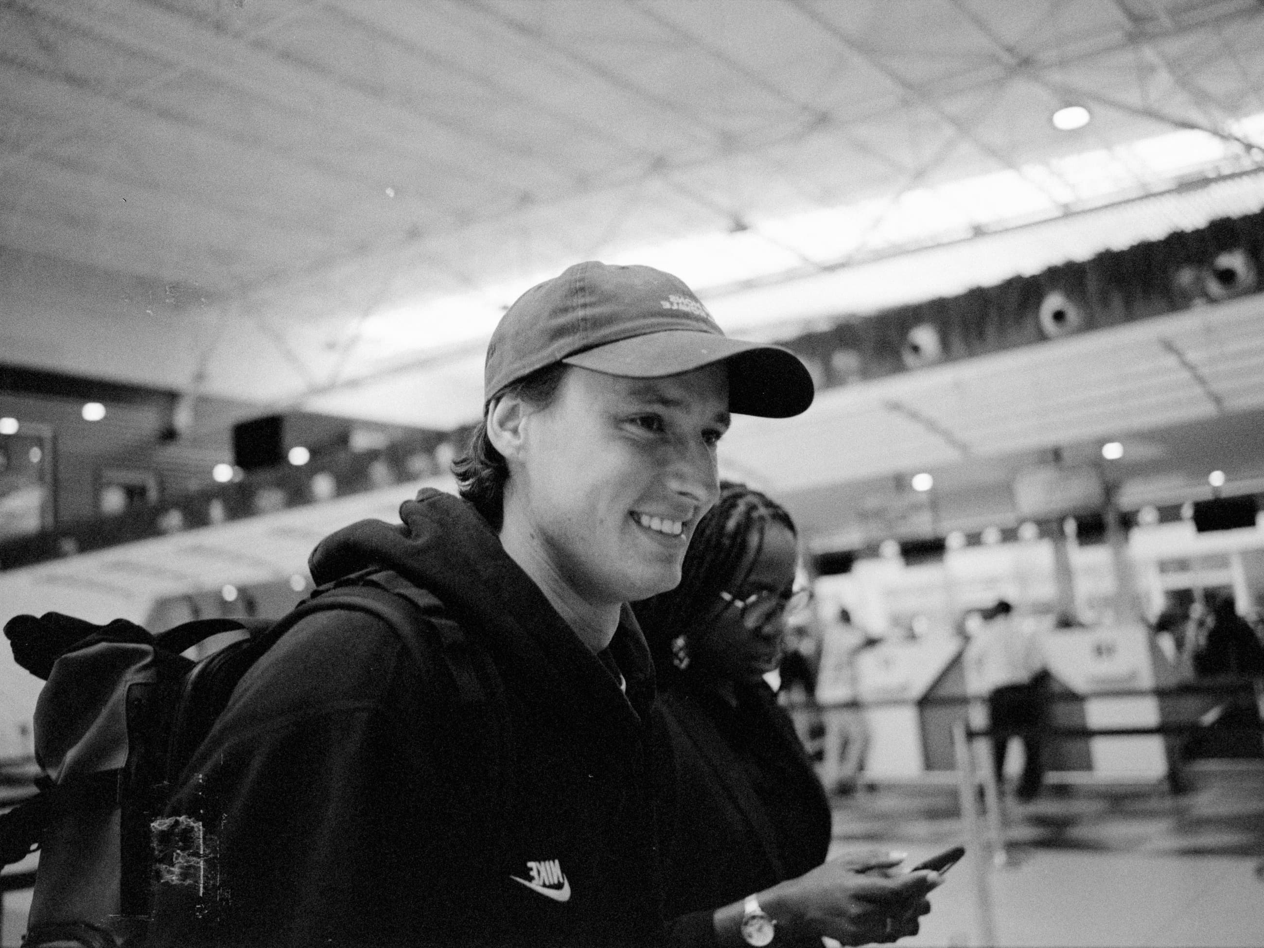 Sam Morgan smiling at an airport, backpack loaded, departing on assignment