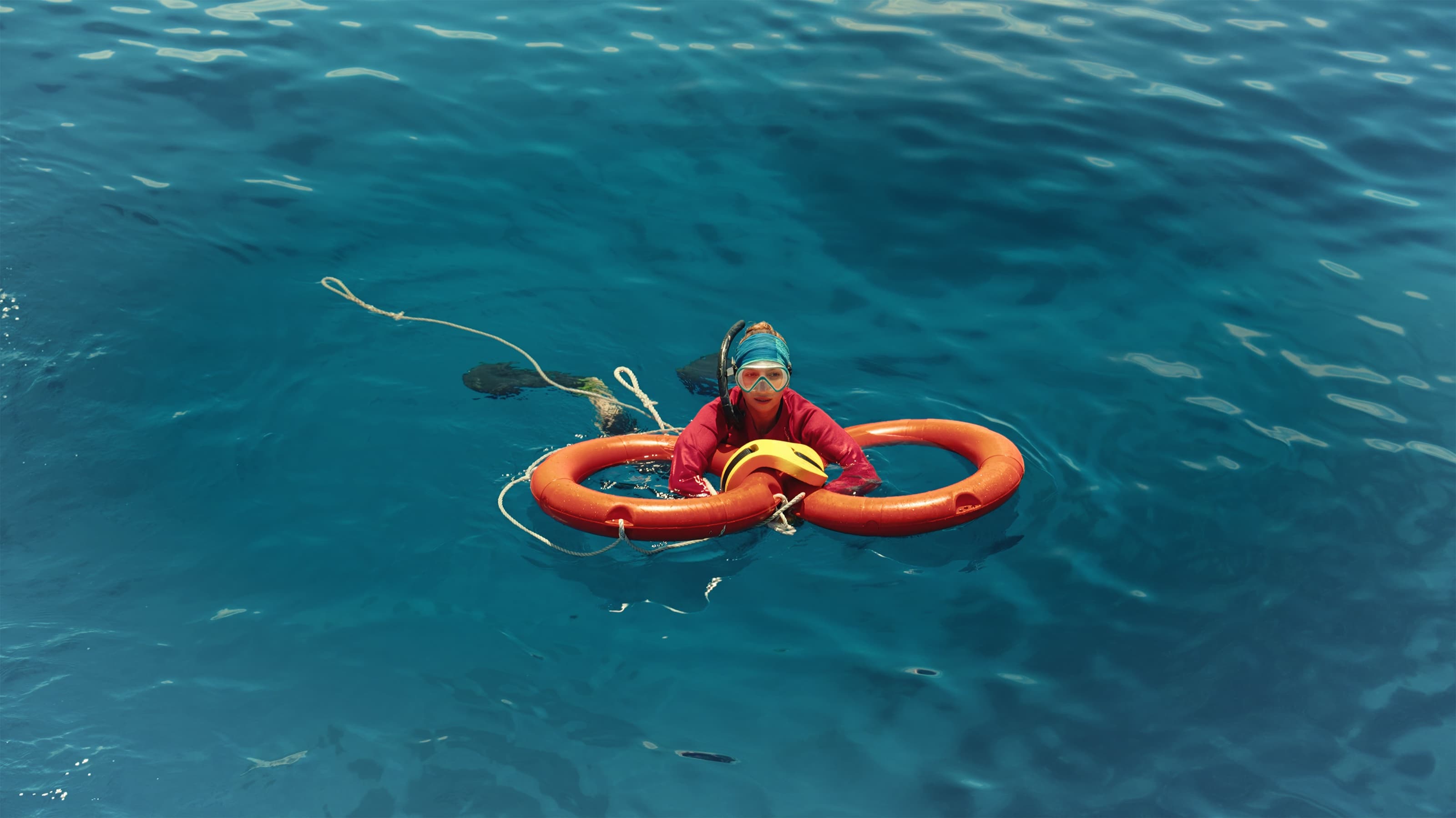 A snorkeler resting in a life ring on calm blue water