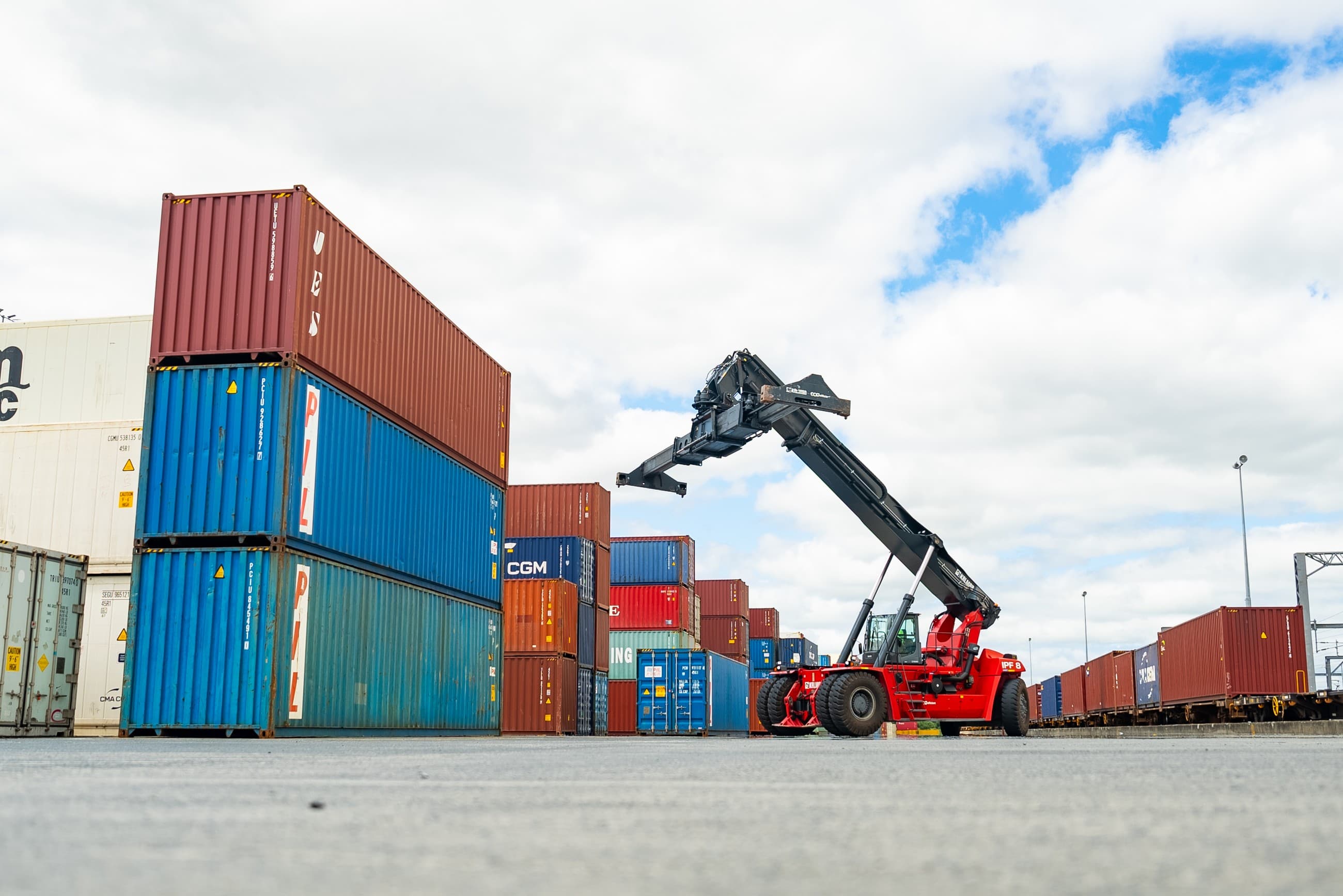 Reach-stacker moving a container beside a loaded freight train
